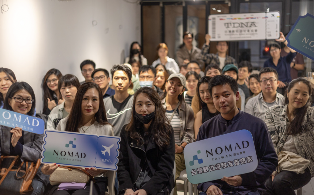 TDNA community gathering at a Digital Nomadic Badge promotion event, attendees holding Nomad Taiwan and Digital Nomad-Friendly Venue signs
