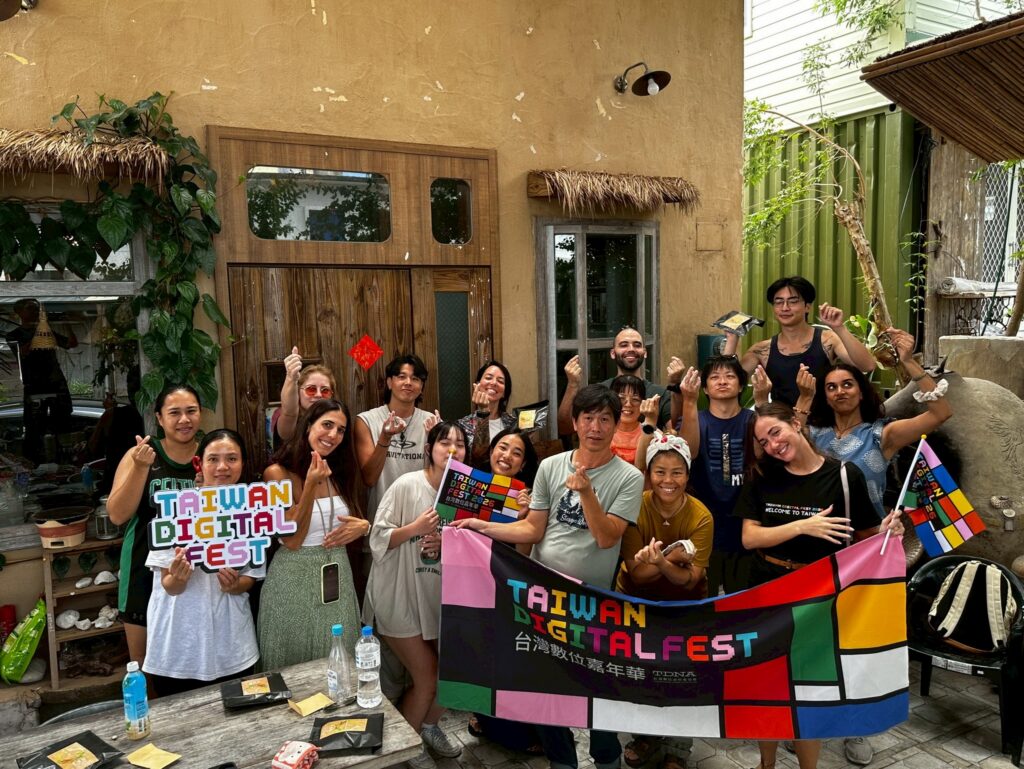 TDF 2026 參與者與在地夥伴於手作工作坊後手持台灣數位嘉年華旗幟合影